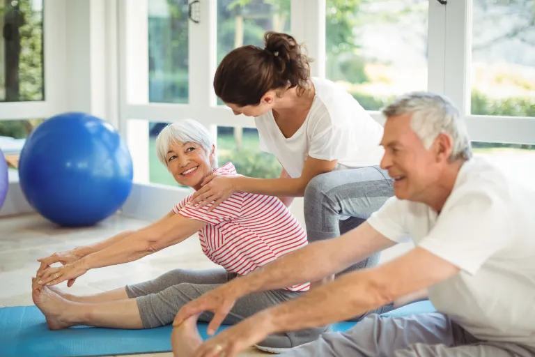 Senior Fit Club Services Female trainer assisting senior couple in performing exercise at home